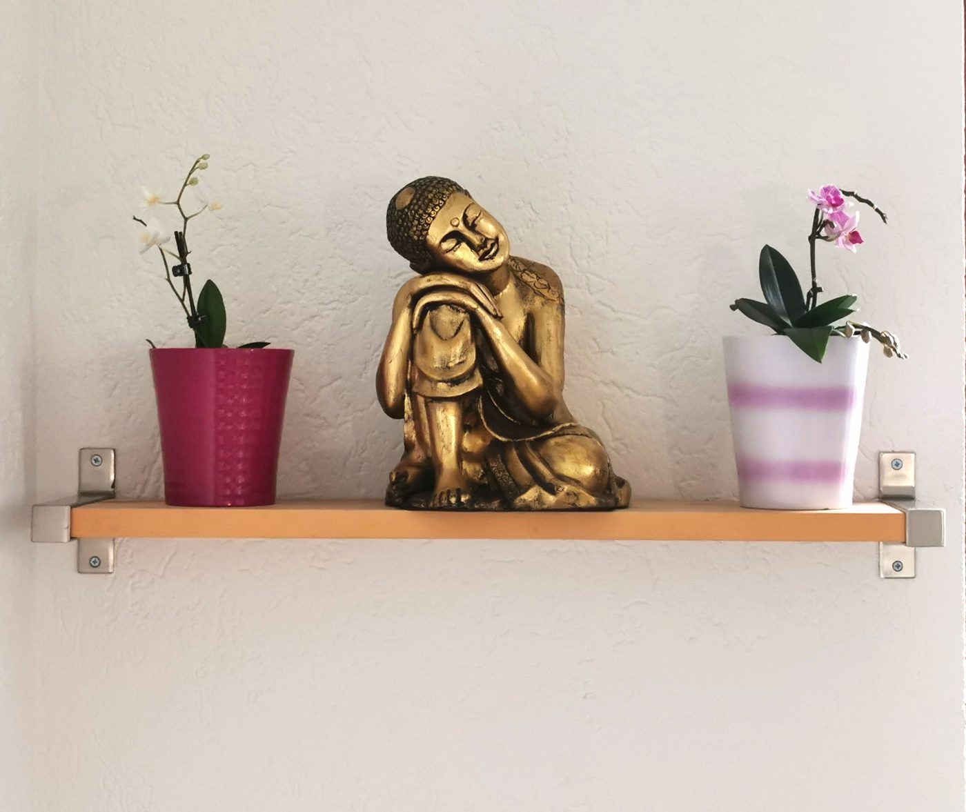 Goldene Buddha-Figur zwischen zwei Orchideen auf einem Regal